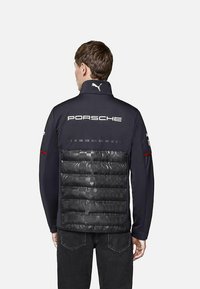 Kurtka marki Porsche i Puma z czarną izolowaną tylną częścią i granatowym przodem. Posiada wysoki kołnierz i ściągacze przy rękawach.