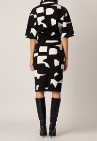 Černobílé vzorované šaty s krátkými rukávy, přiléhavým střihem a délkou po kolena, doplněné černými kozačkami sahajícími ke kolenům.
