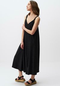 Czarna, bezrękawnikowa sukienka maxi z dekoltem w serek, wykonana z miękkiego materiału, charakteryzująca się luźnym krojem i rozszerzającą się spódnicą, zestawiona z czarnymi sandałami na platformie z paskami.