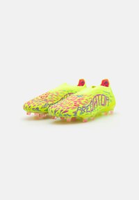 Bright yellow soccer cleats featuring a leopard print design, textured upper, and pink accents. Equipped with translucent conical studs.