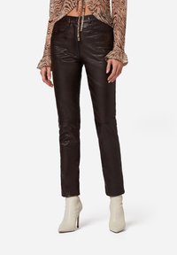 Zwarte leren broek met een slim fit, met een gladde textuur en minimale stikdetails. Gecombineerd met witte hakken.