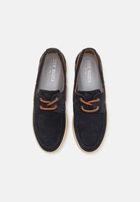 Navy suede slip-on shoes with a tan leather accent, featuring a round toe, stitched details, and rubber sole. Interior has a gray lining.