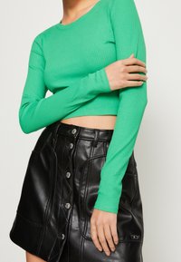 Groene geribbelde langslijfscrop top gecombineerd met een zwarte faux leren rok met knoopdetails en zijzakken.