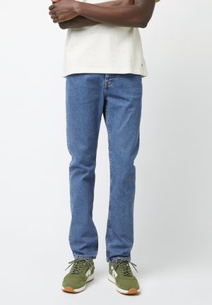 Jeans in denim blu con vestibilità dritta, lavaggio medio e leggera scollatura. Abbinati a sneaker verde e bianche per un contrasto.