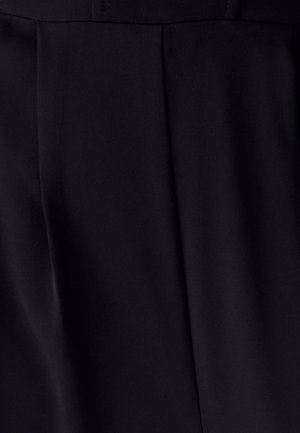 Nahaufnahme von schwarzem Stoff mit vertikalen Falten und subtiler diagonaler Textur in sanfter Beleuchtung.