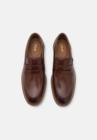 Braune Lederloafer mit glatter Oberfläche, gesteppten Details, doppelten Riemenakzenten und einer gepolsterten Innensohle. Leichte Gummisohle für zusätzlichen Komfort.