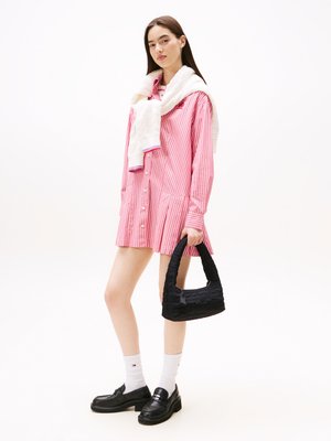 Robe chemise oversized rayée rose avec des boutons, associée à un pull blanc sur les épaules, un sac à main matelassé noir et des mocassins noirs.