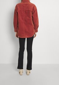 Camisa de pana roja con cuello y puños abotonados, combinada con pantalones acampanados negros y zapatos beige de tacón ancho.
