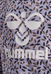 Fliederfarbener Stoff mit floralem Muster, das grüne und braune Blätter zeigt, akzentuiert durch ein großes weißes Logo mit der Aufschrift "hummel" am unteren Rand.