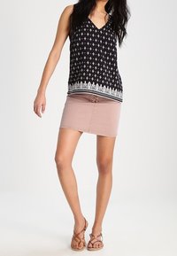 Top senza maniche nero con motivi floreali bianchi, design a V e orlo accentuato. Abbinato a una gonna rosa chiaro e sandali marroni con cinturini.