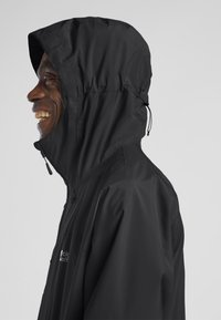 Schwarze wasserdichte Jacke mit hohem Kragen und verstellbarem Kapuze. Glatte Textur, Frontreißverschluss und elegantes Design. Logo auf der Brust.