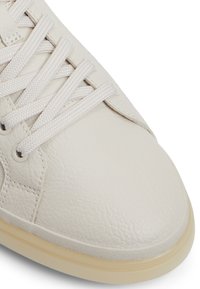 Sneaker bianco in pelle con finitura testurizzata, occhielli rotondi per i lacci, lacci bianchi piatti e suola in gomma color crema.