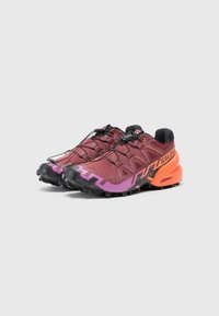 Trailrunning-skor med maroon-överdel, svarta snören och en gradientaccent från orange till lila. Har en texturerad sula för bra grepp.