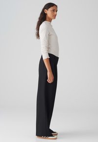 White long-sleeve top with scalloped cuffs, paired with high-waisted black wide-leg trousers and black, white-accented sneakers.