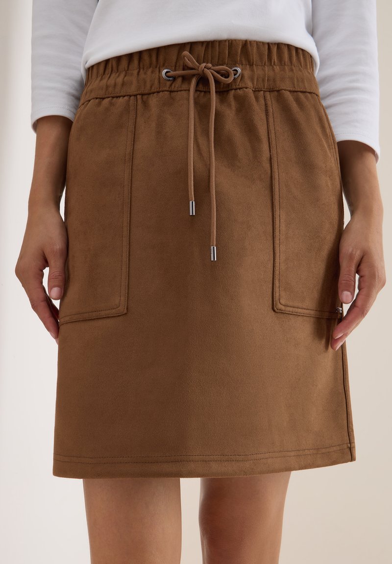 Jupe en daim marron avec une taille élastique et un cordon de serrage. Deux poches avant et des détails de couture soignés. Texture lisse sur l'ensemble.