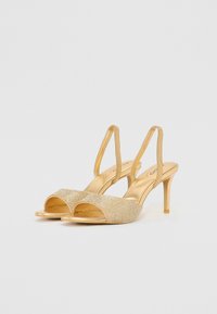 Zlaté slingback podpatky s odhalenými prsty, zdobené texturovaným, třpytivým předním dílem. Mají jehlový podpatek a štíhlé pásky.