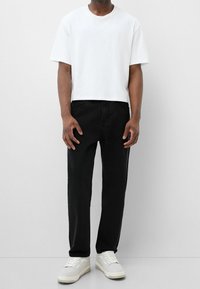 Bílá bavlněná tričko s krátkým rukávem, kombinované s černými džíny a bílými teniskami. Jednoduchý, rovný střih, minimální detaily.