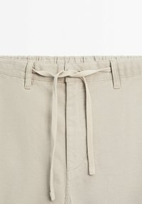 Beige shorts med elastisk talje, udstyret med snoretræk og sømdetaljer, lavet i et tekstureret og let materiale.