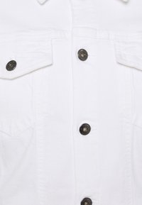 Giacca di jeans bianca con chiusura a bottoni, due tasche sul petto con pattina e bottoni metallici. Il tessuto ha una finitura liscia e strutturata.