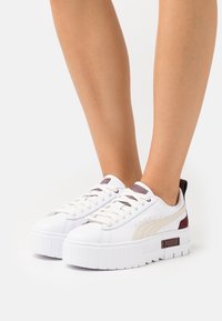 Weiße Plattform-Sneaker mit strukturierten Gummisohlen, Schnürverschlüssen und seitlichen Akzenten in Burgunderrot und Beige. Mit PUMA-Logo an der Ferse.
