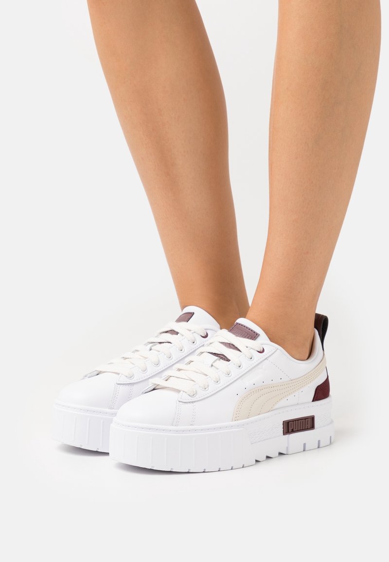 Weiße Plattform-Sneaker mit strukturierten Gummisohlen, Schnürverschlüssen und seitlichen Akzenten in Burgunderrot und Beige. Mit PUMA-Logo an der Ferse.