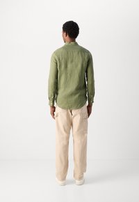 Cămașă verde din in cu guler, mansete cu nasturi și o margine curbată, asortată cu pantaloni cargo bej cu buzunare laterale și un croi relaxat.