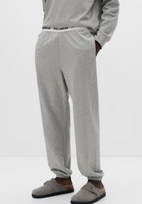 Szare spodnie dresowe z elastycznym paskiem w talii, z czarnym logo „PULL&BEAR”. Miękka tekstura i luźne dopasowanie z mankietami przy kostkach oraz kieszeniami bocznymi.