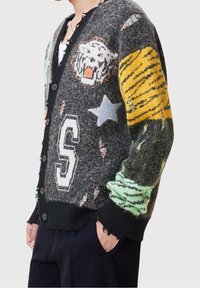 Pletený cardigan s šedým základem, barevnými zvířecími grafikami a záplatami. Opotřebované okraje a černé knoflíky dotvářejí design.