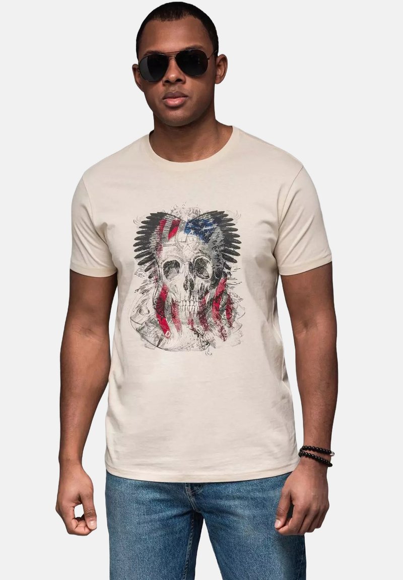 Beige kortærmet t-shirt med et kraniumdesign og røde og blå striber, der minder om et flag, glat stof og en klassisk pasform.