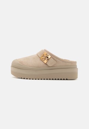 Mule platform in suede beige con una suola spessa e testurizzata, caratterizzati da un prominente accento in metallo dorato sulla fascia regolabile.