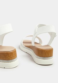 Białe sandały z syntetycznej skóry z drewnianymi obcasami, zdobione przezroczystym akcentem z dżetów wzdłuż krawędzi oraz teksturowaną podeszwą.