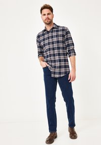 Navy- und weiße karierte Button-Up-Bluse mit Kragen, kombiniert mit dunkelblauen Jeans und braunen Schnürstiefeln. Das Hemd verfügt über eine Brusttasche.