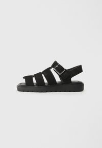 Sandalias de ante negro con tres correas anchas y hebilla ajustable. Suela de goma gruesa con patrón texturizado para mayor agarre. Vista lateral.