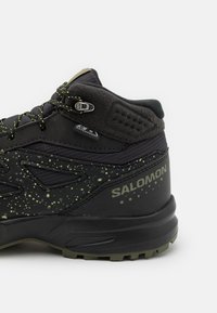 Czarny but hikingowy z zielonym, nakrapianym wzorem, wodoodporny materiał, teksturowana cholewka, wzmocniony obcas i wyraźne logo marki.