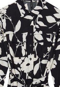 Abito camicia a fiori in bianco e nero con colletto, due tasche sul petto, chiusura con bottoni e una cintura in tessuto in vita.