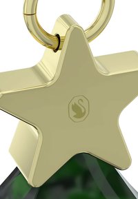 Złota zawieszka w kształcie gwiazdy o błyszczącym wykończeniu, z logo łabędzia i metalowym pierścieniem do zawieszenia. Podstawa ma zielony odcień.