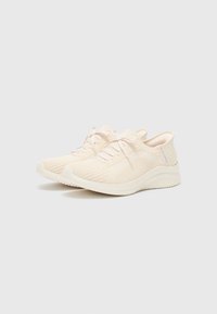 Hellbeige Sneaker mit einem Strickoberteil, das ein Wellenmuster aufweist, tonalen Schnürsenkeln und einer dicken, strukturierten Sohle. Minimalistisches Design mit sanften Akzenten.
