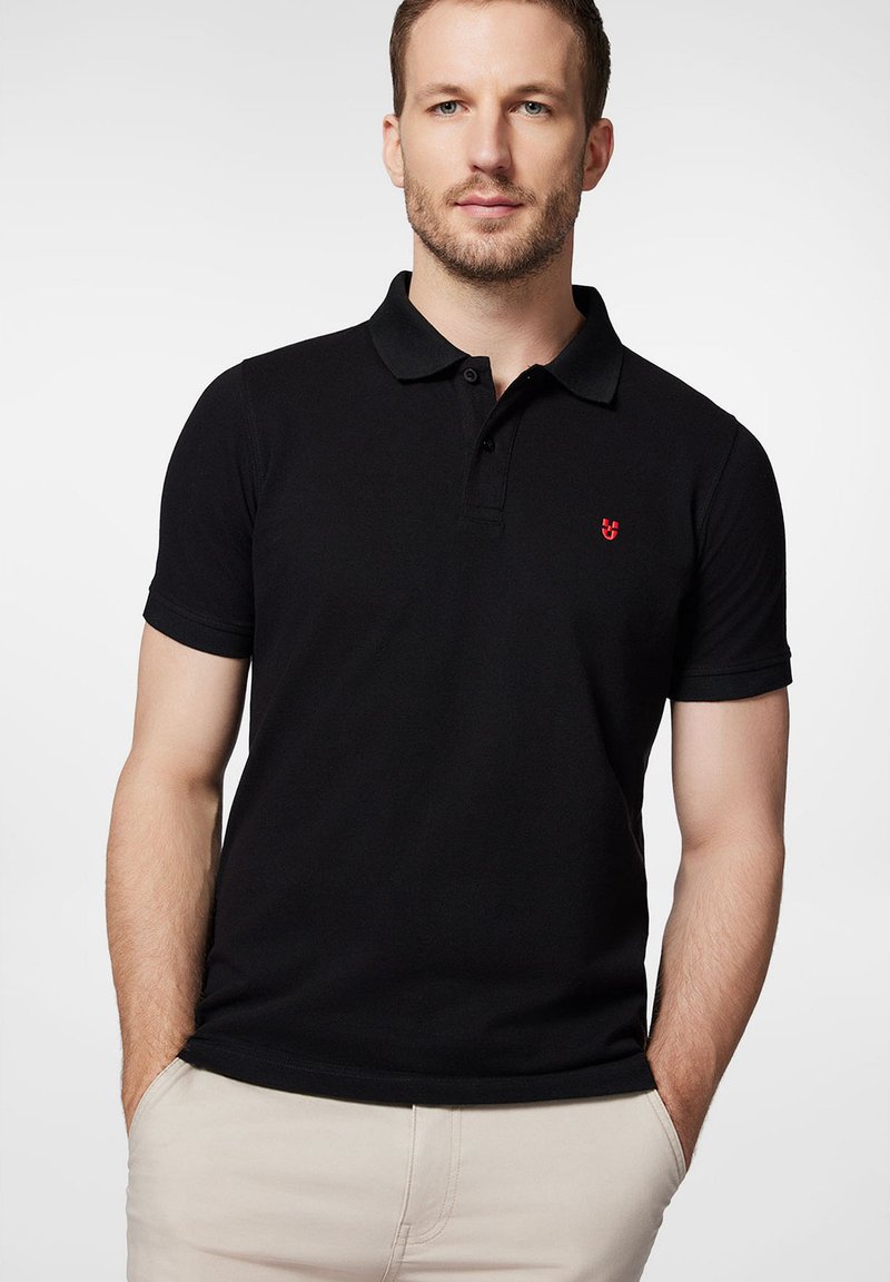 Czarny polo z krótkim rękawem, z klasycznym kołnierzykiem i małym czerwonym logo na piersi. Gładka bawełniana tekstura, dopasowany krój.