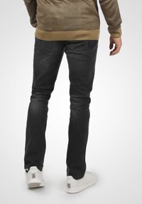 Jeans oscuros de corte slim con una textura suave y detalles mínimos. Combinados con zapatillas blancas que tienen una franja de color en el talón.
