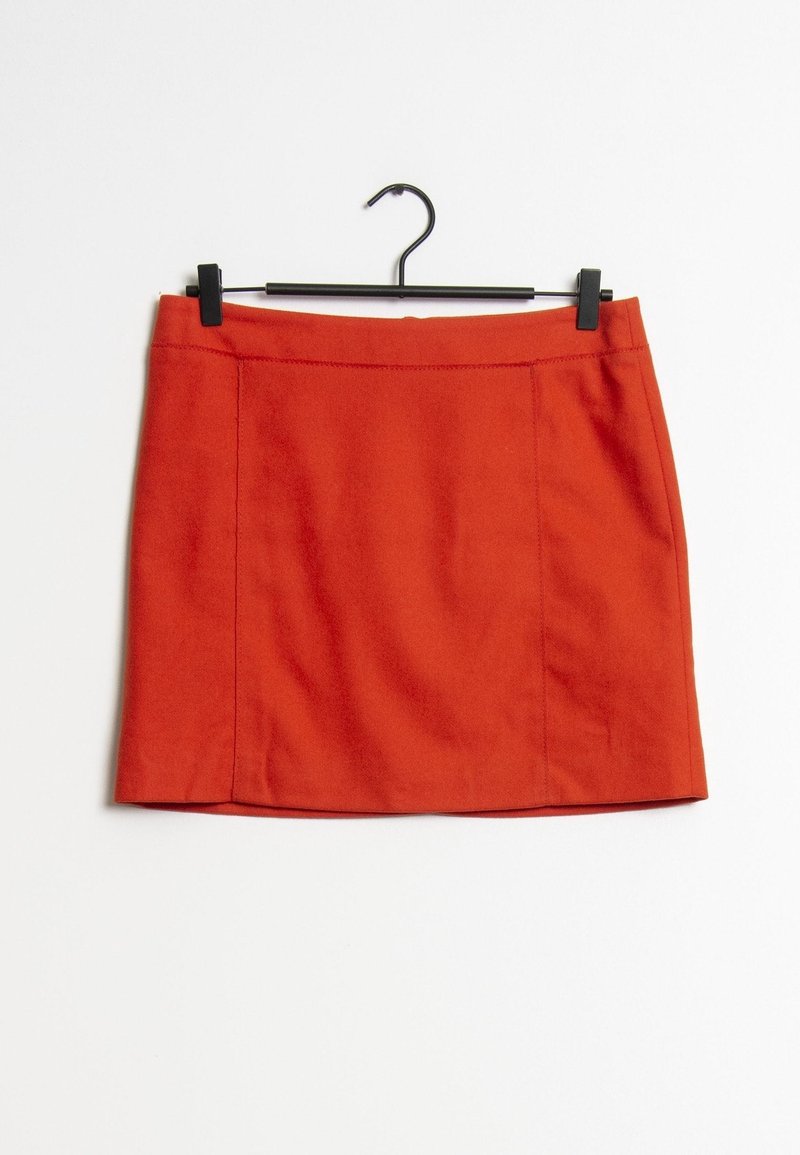 Mini-jupe rouge suspendue à un cintre noir sur fond blanc, avec une coupe droite simple et des détails de couture visibles.