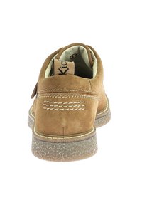 Zapato de ante marrón con forma redondeada, suela de goma y detalles de costura en contraste. La etiqueta de la plantilla indica la talla 37.