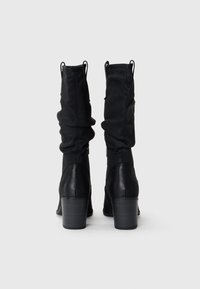 Schwarze Stiefel bis zur Mitte der Wade mit einem lässigen Stoffobermaterial, Lederakzenten und einem klobigen, genoppten Absatz. Reißverschlussdetails an der Seite.