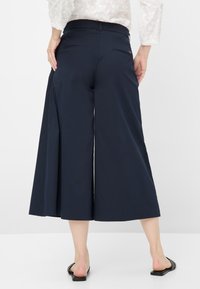 Navy culottes made of lightweight fabric, featuring a wide leg design, subtle back pockets, and a smooth texture. Flat sandals visible.