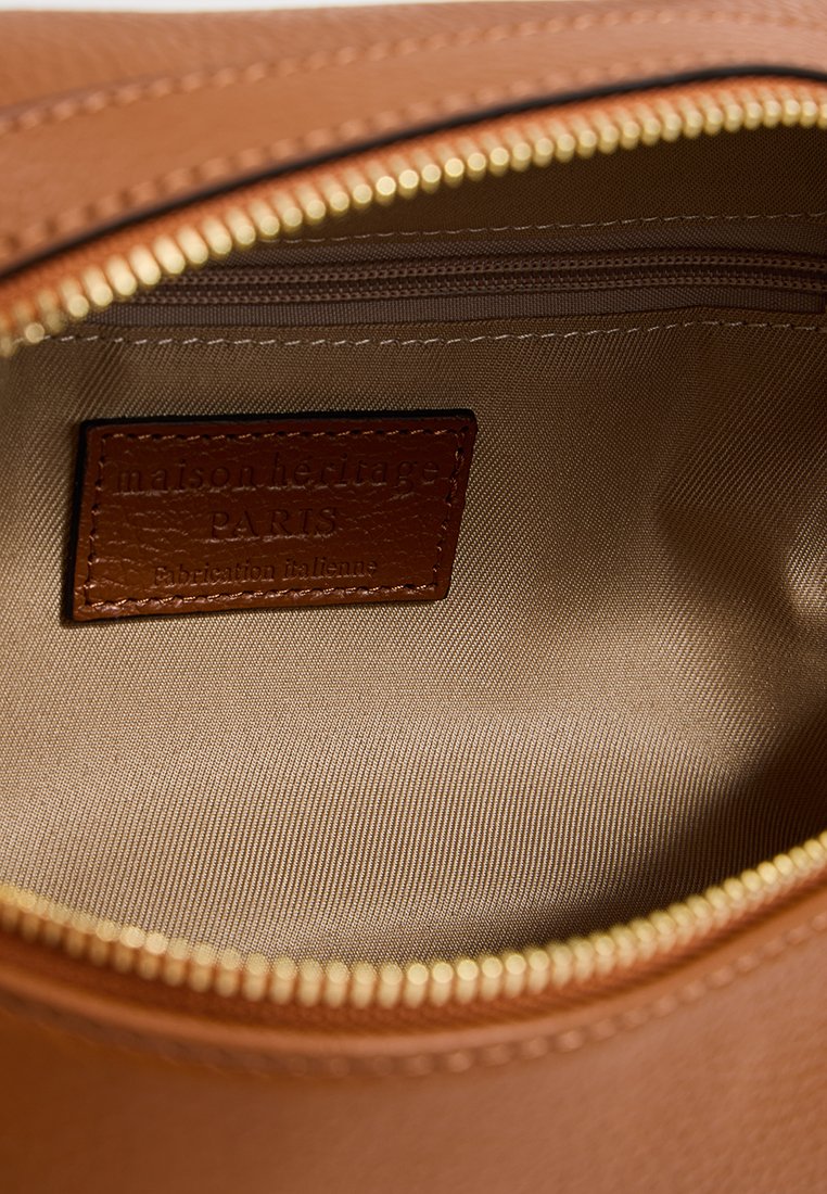 Intérieur d'une pochette en cuir tan avec une doublure beige contrastante. Présente une fermeture éclair et une étiquette en cuir marron avec texte en relief.