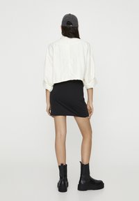 Biała krótka kurtka, czarna dopasowana sukienka, czarne masywne botki o fakturowanej powierzchni oraz szara czapka noszona do tyłu.