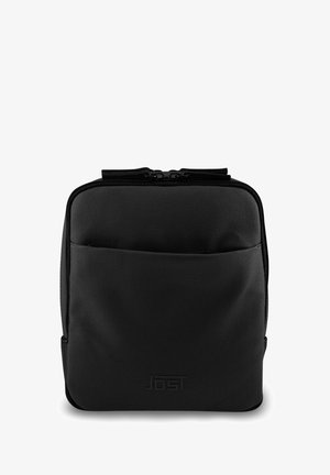 Sac à dos carré noir en tissu texturé ; il dispose d'une fermeture éclair sur le dessus et d'une poche avant. Le logo de la marque est embossé sur le devant.