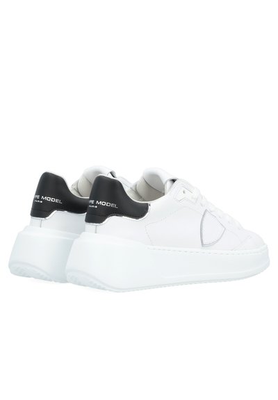 Le sneakers in pelle bianca presentano una suola spessa bianca, con un tallone nero e dettagli del logo argentato. Texture liscia con elementi di design arrotondati.