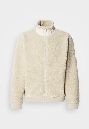 Kermanvärinen fleecetakki, jossa korkea kaulus ja täysi vetoketju. Ominaisuuksina teksturoitu kangas ja resorit hihansuissa. Minimalistinen design.