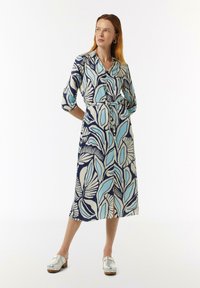 Langes Kleid aus einem dunkelblauen Stoff mit einem großen Blattmuster in Hellblau und Creme. Mit beiliegendem Gürtel und Dreiviertelärmeln.