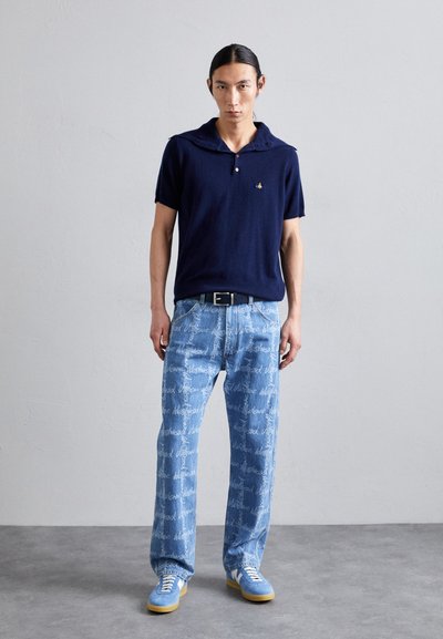 Navy knit polo shirt with a wide collar, paired with light blue denim jeans featuring white text patterns. Blue sneakers with yellow soles.